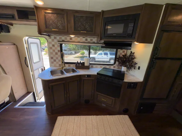 RV rental showing a functional kitchenette with a double sink, microwave, stove, and wood cabinetry in a clean, modern interior.. Coachmen Freelander 2018