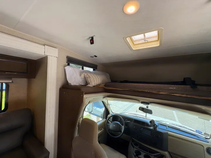 View inside an rv rental, featuring a cozy cab-over bunk, the driver's cockpit with a steering wheel, and an overhead vent.. Coachmen Freelander 2018