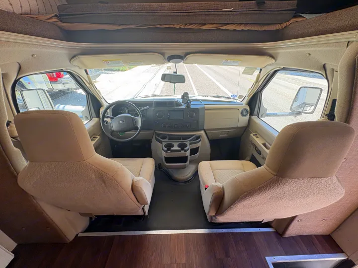 Inside an RV rental: View of the cockpit from the living area, showing driver/passenger seats, dashboard, and overhead bunk.. Coachmen Freelander 2018