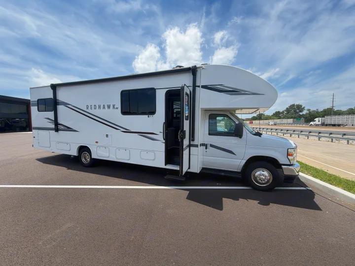 White Class C Redhawk RV parked by a highway, door open, suggesting an upcoming RV rental journey.. Jayco Redhawk SE 31FF 2026