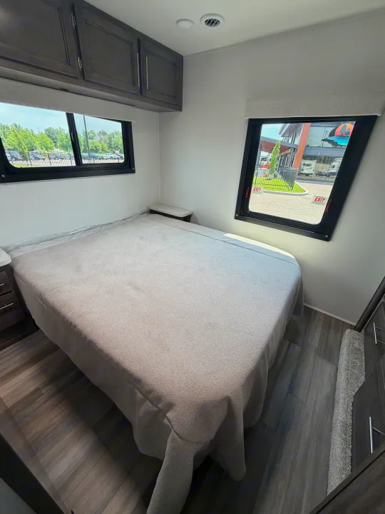 This RV rental bedroom features a comfortable bed, dark wood cabinets, and two large windows with outside views.. Jayco Redhawk SE 31FF 2026