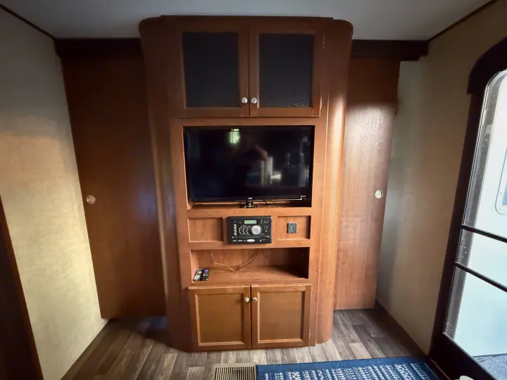 RV rental interior featuring a wood-paneled entertainment center with a TV, stereo, and storage cabinets, plus an entry door.. Keystone RV Hideout Luxury 2017