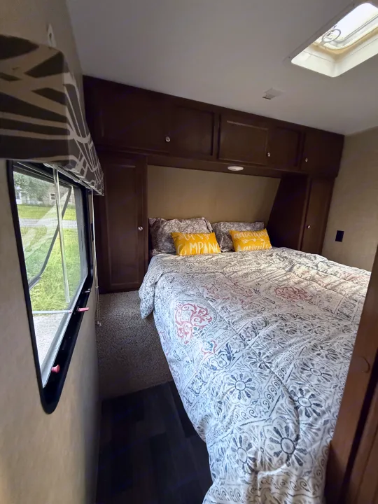 Enjoy a comfortable RV rental bedroom featuring a bed, yellow pillows, overhead cabinets, window view, and skylight.. Keystone RV Hideout Luxury 2017