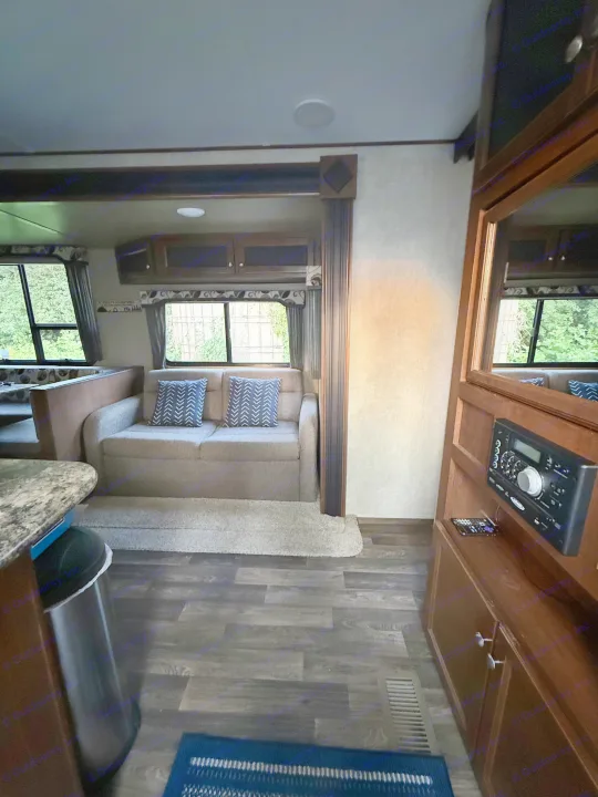 This RV rental offers a cozy interior with a gray sofa, blue pillows, dinette, and media system.. Keystone RV Hideout Luxury 2017