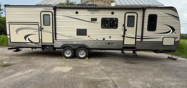 Side view of a Hideout by Keystone travel trailer RV rental, with an awning, two doors, and dual axles, parked on concrete.. Keystone RV Hideout Luxury 2017