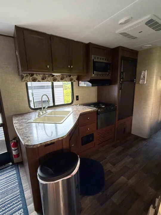 This RV rental galley features dark cabinets, a sink, stove, microwave, and fridge, ready for your adventures.. Keystone RV Hideout Luxury 2017