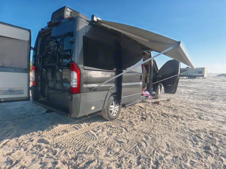 Enjoying the sun with an RV rental campervan on a sandy beach. Awning deployed, doors open for beachside relaxation.. Thor Sequence 2022