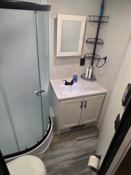 Compact RV rental bathroom: features curved frosted shower, white vanity with sink, mirror, and multi-tier corner caddy.. JAYCO JAY FLIGHT SLX 2026