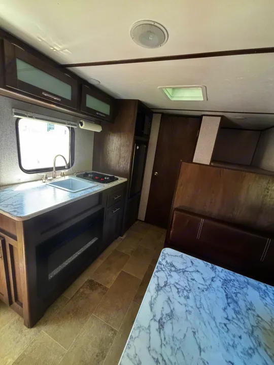 RV rental interior featuring a kitchenette with sink, stove, and fridge, plus a dining booth with a marble table.. Dutchmen Coleman Lantern LT 2021