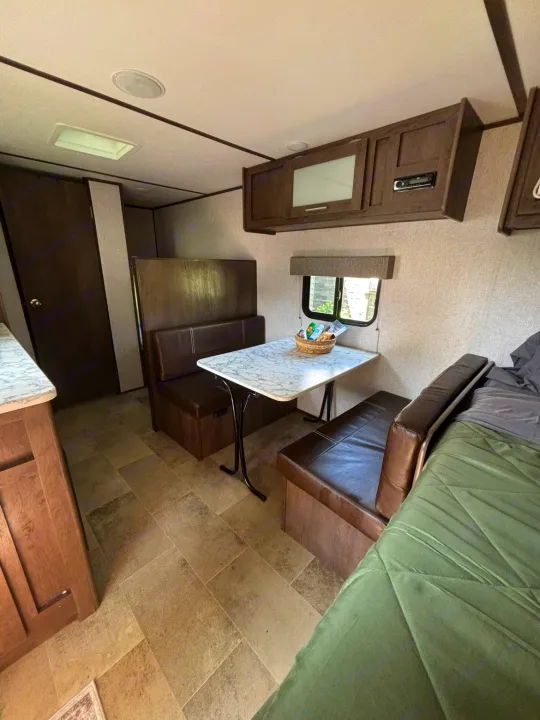 Rv rental interior: compact dinette, booth seats, marble-top table, overhead cabinets, and sleeping area.. Dutchmen Coleman Lantern LT 2021