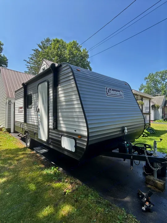 This gray and black Coleman travel trailer, perfect for an rv rental, sits parked on a driveway with its side door open.. Dutchmen Coleman Lantern LT 2021