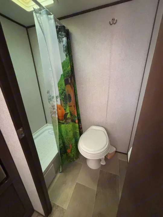 Compact RV rental bathroom featuring a shower with a whimsical themed curtain, and a standard toilet.. Dutchmen Coleman Lantern LT 2021