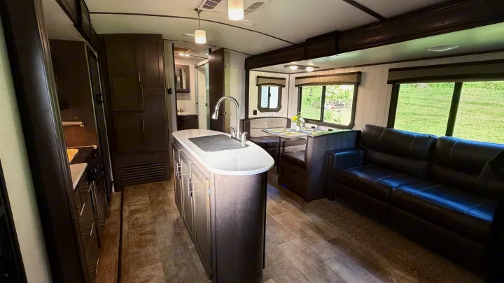 RV rental interior featuring a modern kitchen island with sink, dining booth, dark leather sofa, and a bathroom entrance beyond.. Crossroads RV Sunset Trail Grand Reserve 2017