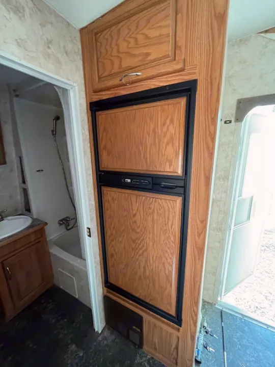 RV rental interior: Compact kitchen with wood-paneled fridge/freezer and cabinets, next to a bathroom with a sink, tub, and shower.. Eclipse Recreational Vehicles Attitude 2007