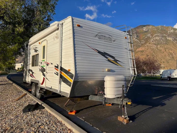 White travel trailer RV rental, parked with stabilizers and a propane tank, set against a backdrop of mountains.. Eclipse Recreational Vehicles Attitude 2007