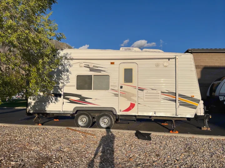 White travel trailer RV rental with bold graphics, parked on pavement next to gravel. Visible under a blue sky.. Eclipse Recreational Vehicles Attitude 2007