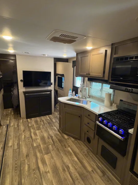 Modern RV rental interior: kitchen with stove & microwave, living area with TV, and stylish wood-look flooring.. Starcraft Super Lite 2022