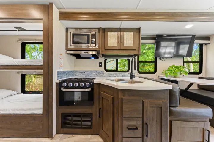 Modern RV rental interior showcasing a compact kitchen with stove, microwave, sink, cozy bunk beds, and a dinette area.. Coachmen Pursuit 2024