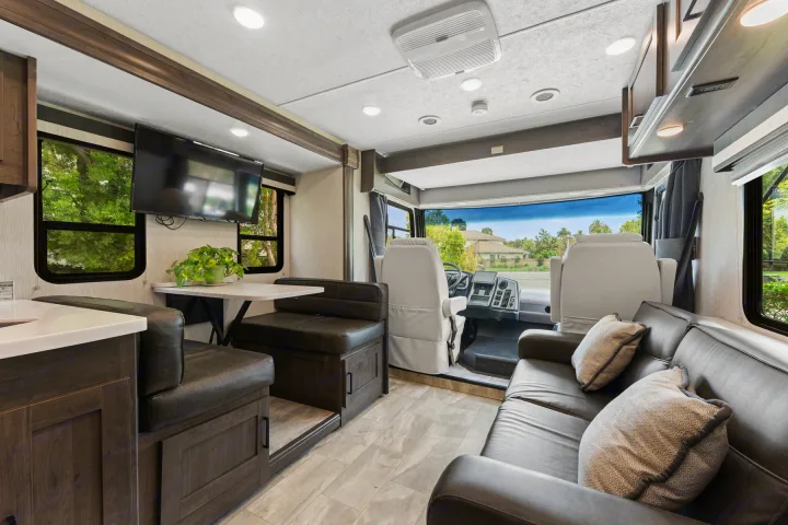 This spacious RV rental interior features a comfortable living area, dinette, and bright cockpit with scenic views for your journey.. Coachmen Pursuit 2024