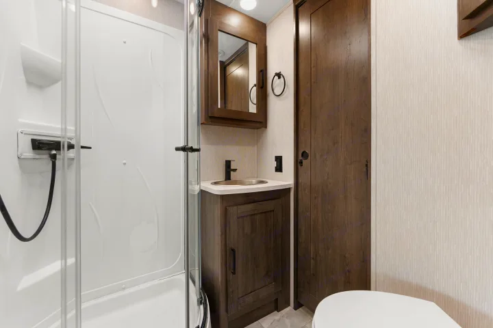 Modern RV rental bathroom featuring a shower, sink vanity, and toilet. Compact and functional for your travels.. Coachmen Pursuit 2024