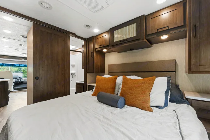 Spacious RV rental bedroom with a comfy bed, overhead storage, and a sliding door leading to the bathroom and cockpit.. Coachmen Pursuit 2024