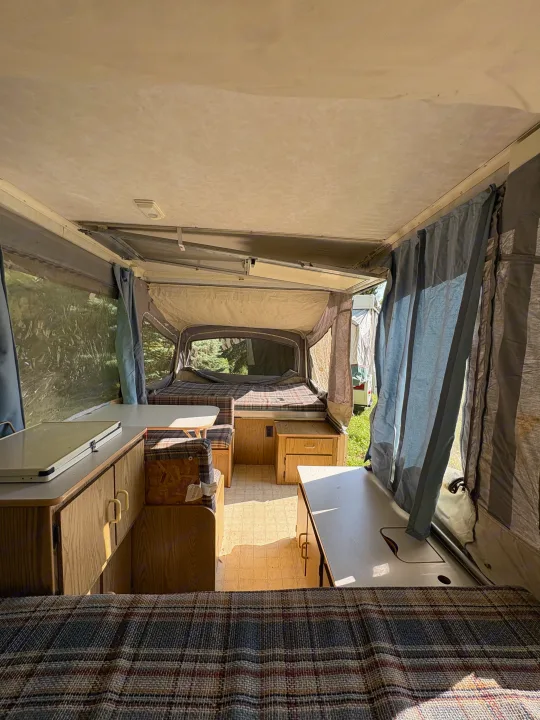 View inside a cozy pop-up camper with plaid beds, dining area, and cabinetry. Ideal for your next RV rental adventure.. Coleman Destiny Roanoke 1991
