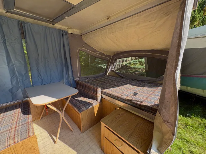 Cozy vintage pop-up camper interior, featuring a plaid bed, dinette, and blue curtains. Perfect for your next RV rental adventure.. Coleman Destiny Roanoke 1991