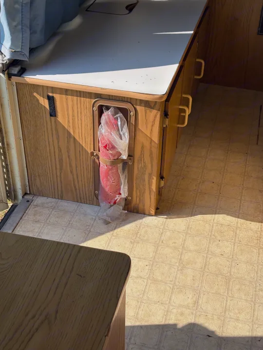 Inside this RV rental, a bagged red fire extinguisher is secured in a wood-grain cabinet. Light-colored patterned linoleum flooring is visible.. Coleman Destiny Roanoke 1991