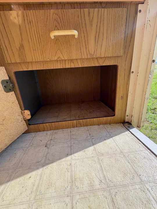 RV rental storage area: Open wood-grain cabinet, drawer, and dirty patterned linoleum floor, highlighting interior condition.. Coleman Destiny Roanoke 1991