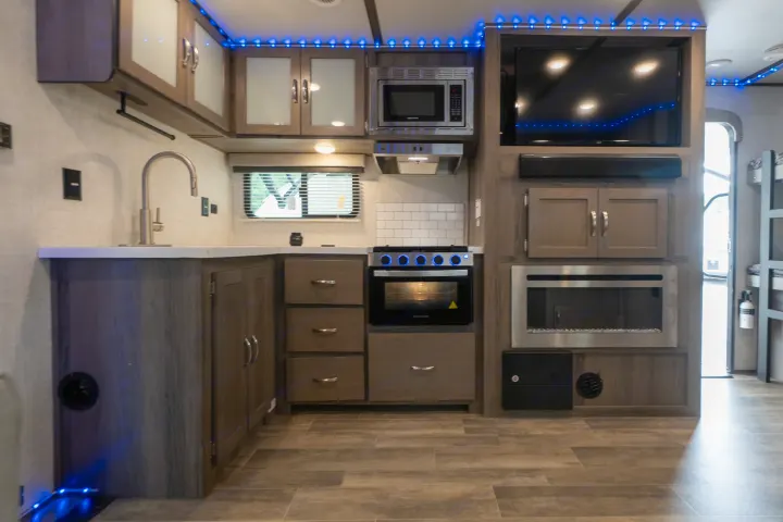 Modern RV rental kitchen with sink, microwave, stove, TV, cabinets, and ambient blue LED lighting.. Gulf Stream Envision 2021