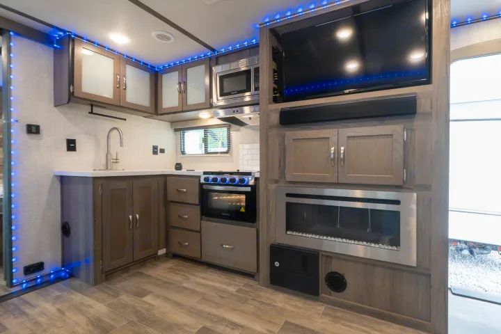 Modern rv rental kitchen & living space: blue accent lights, stove, microwave, sink, TV, and electric fireplace visible.. Gulf Stream Envision 2021