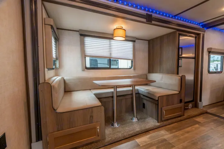 RV rental interior featuring a modern U-shaped dinette, window with blinds, and cool blue LED ceiling lights.. Gulf Stream Envision 2021