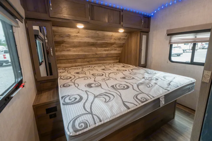 Experience comfort in this RV rental bedroom: queen bed, wood details, overhead storage, and ambient lighting.. Gulf Stream Envision 2021
