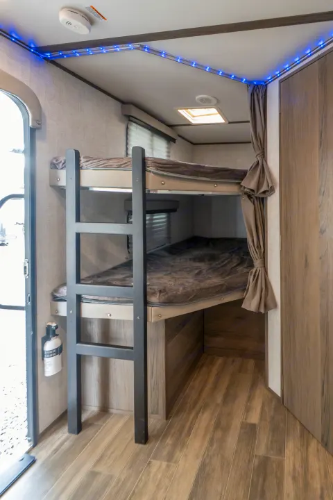 Inside an RV rental: a comfortable bunk bed area with a ladder, blue LED lights, and privacy curtains.. Gulf Stream Envision 2021