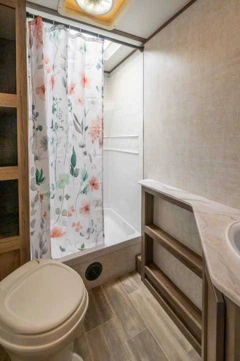 Compact RV rental bathroom with a floral shower, toilet, and vanity. Features wood-look floor and light walls.. Gulf Stream Envision 2021