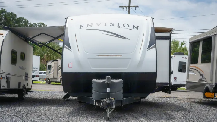 Front of a white Envision by Gulf Stream travel trailer, available as an RV rental, on a gravel lot with other units.. Gulf Stream Envision 2021
