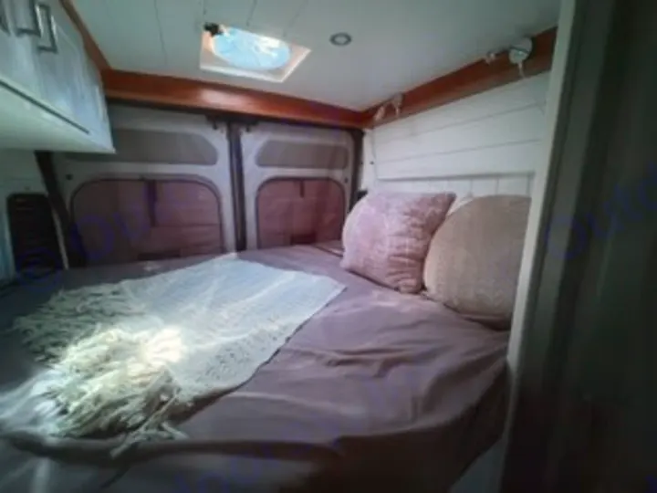 Cozy RV rental bed with plush pillows and blanket in a camper van interior. Perfect for your next van life adventure.. Custom Promaster 2500 2025