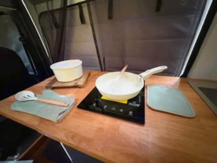 Cooking in your RV rental! Compact kitchen counter with an induction cooktop, pan, bowl, and cooking essentials.. Custom Promaster 2500 2025