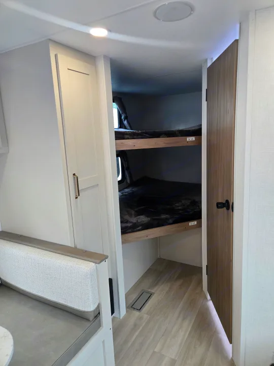 Cozy rv rental interior with bunk beds, dark bedding, cabinet, and open wooden door. Perfect for family adventures.. KZ Sportsmen 291BHK 2027