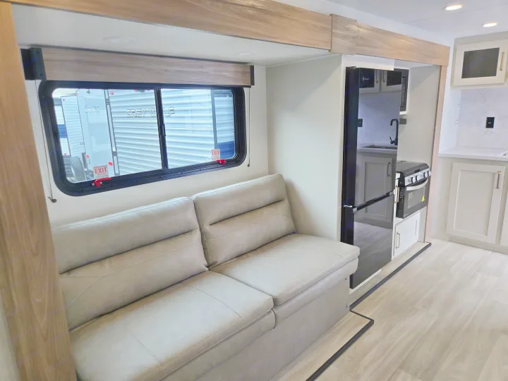 Modern rv rental interior with a cozy sofa, large window view, and a glimpse into the kitchen area.. KZ Sportsmen 291BHK 2027