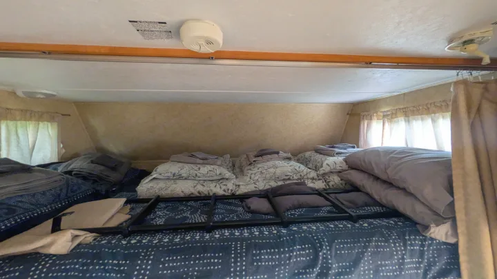 Cozy RV rental sleeping area with bunk bed, pillows, blankets, a smoke detector, and curtains.. Forest River Sunseeker 2010