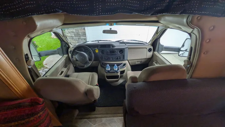 Inside an RV rental: driver's cockpit with steering wheel, dashboard, seats, and water bottles. View of garage outside windshield.. Forest River Sunseeker 2010
