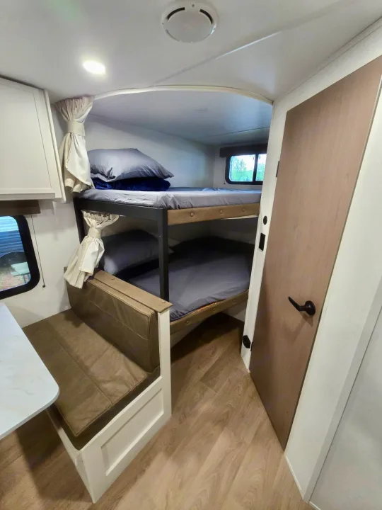 Bright rv rental interior with cozy dual bunk beds, dinette seating, wood-look floor, and large window for family trips.. Grand Design RV Transcend Xplor 26BHX 2027