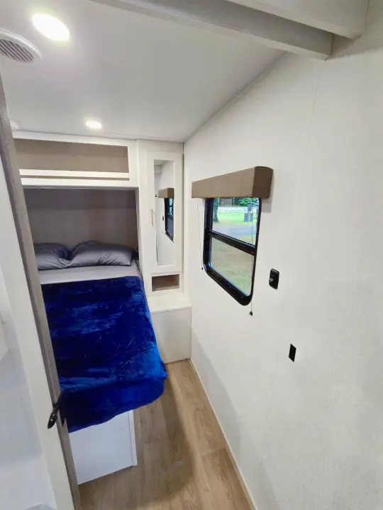 View inside an RV rental, featuring a cozy bunk bed with blue blanket, window, and built-in storage. Ideal for camping comfort.. Grand Design RV Transcend Xplor 26BHX 2027