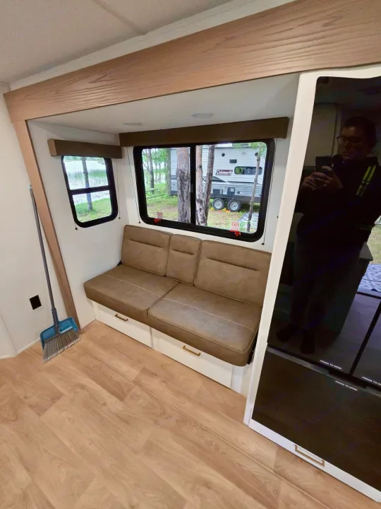 This RV rental interior features a dinette bench with storage, scenic windows overlooking a lake, and light wood floors.. Grand Design RV Transcend Xplor 26BHX 2027