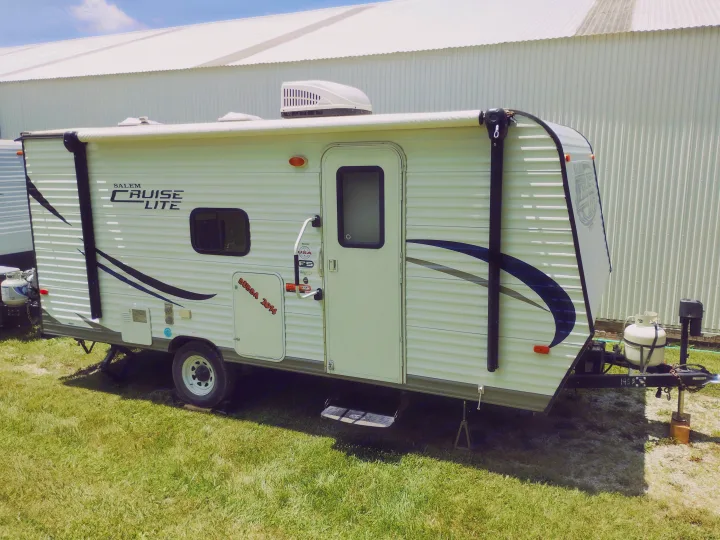 A white Salem Cruise Lite travel trailer, equipped with an AC unit and propane tanks, parked on grass. Ideal for RV rental vacations.. Forest River Salem Cruise Lite 2014