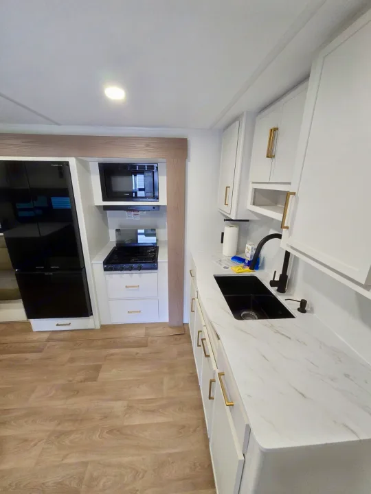 Bright rv rental kitchen featuring white cabinets, black appliances, marble-look counters & wood flooring.. Grand Design RV Transcend Xplor 26BHX 2027