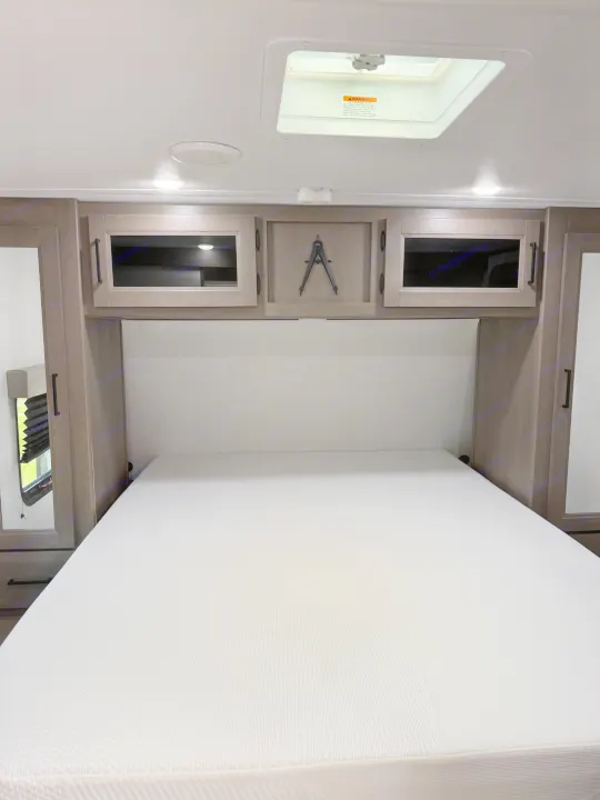 Spacious RV rental bedroom with a comfy mattress, overhead storage cabinets, and a ceiling skylight for natural light.. Grand Design Transcend 2025