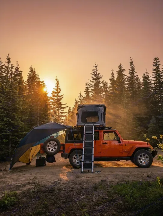 Off-road RV rental setup: Orange Jeep Wrangler with rooftop tent and side awning in a sun-drenched forest at sunset.. Jeep Wrangler 2012