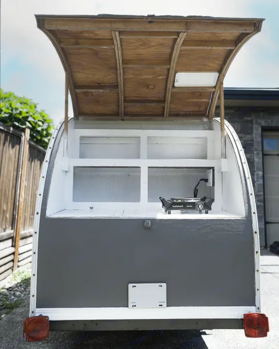Compact **RV rental** trailer, customized with an open service hatch, interior shelves, and a portable stove for mobile use.. Micro-Lite Micro Camper 1987